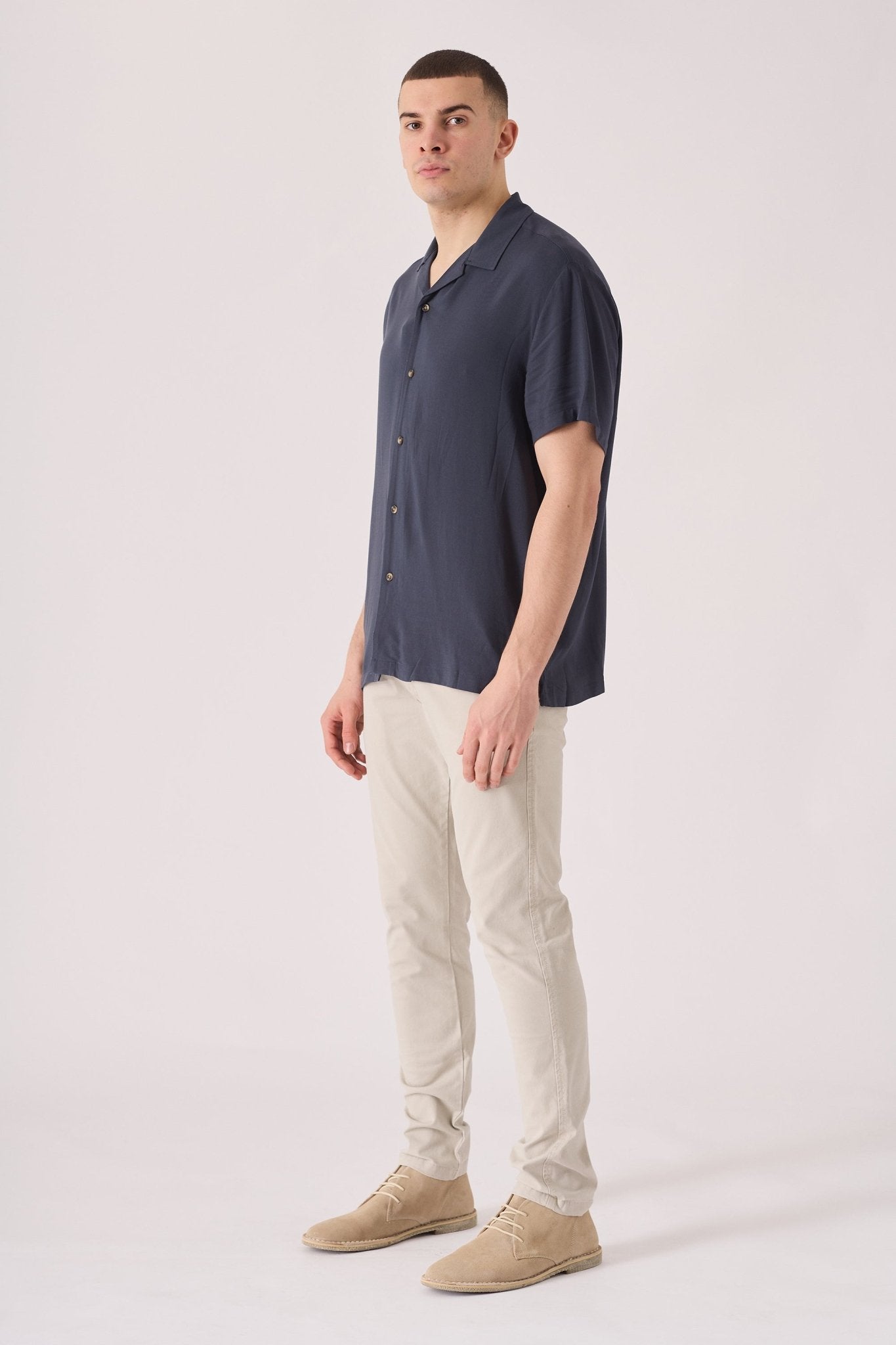 Side view of a man wearing cream chinos slim fit in a studio setting.