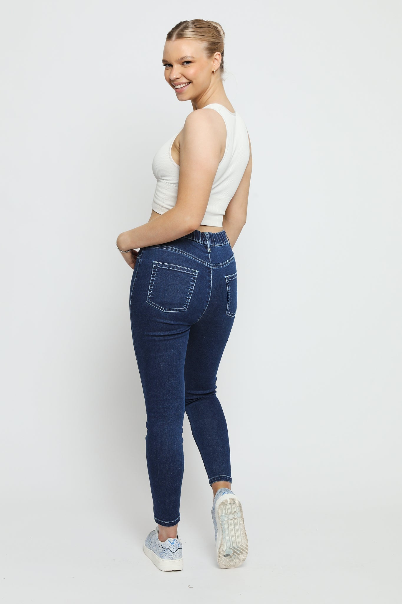 Rear view of a woman wearing slim fit dark blue denim jeggings showing the pocket detail and stretch fabric.