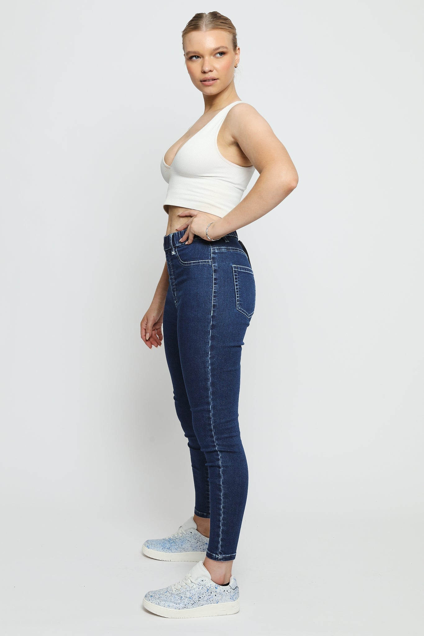 Side view of a woman wearing high-waisted dark blue denim jeggings to show the slim silhouette.
