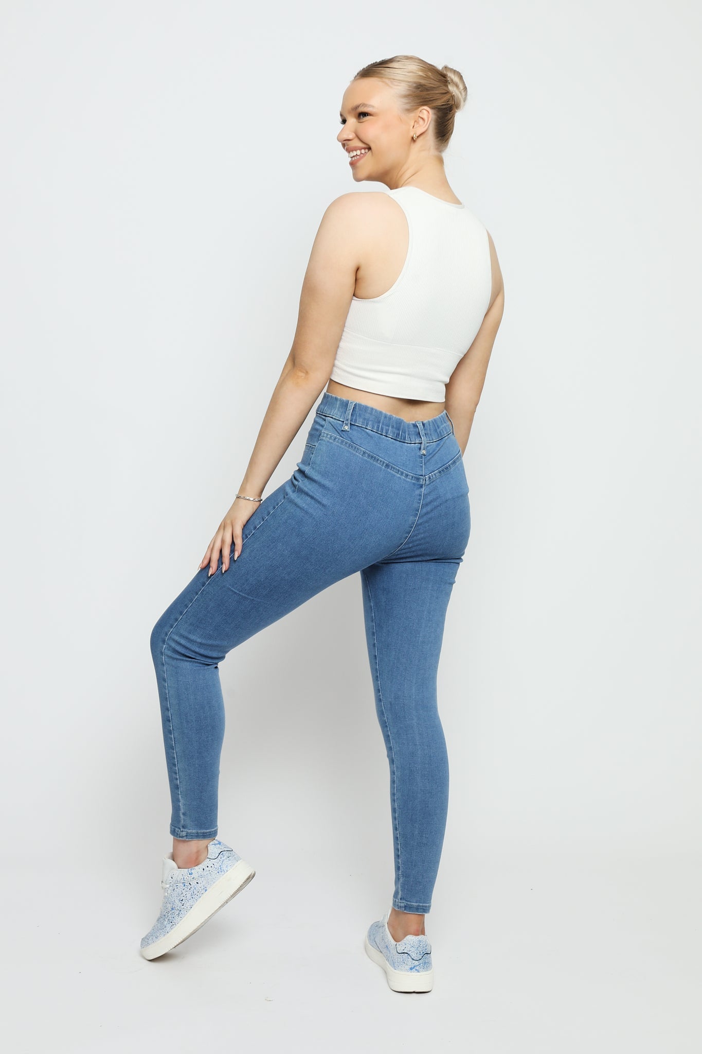 Rear view of a woman posing in slim fit mid blue denim jeggings to show the flexible stretch fabric.