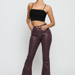 A woman posing in maroon coated skinny bootcut jeans paired with a black crop top.