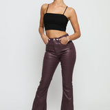 A woman posing in maroon coated skinny bootcut jeans paired with a black crop top.
